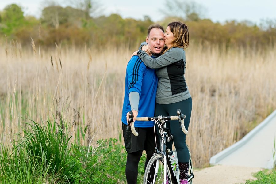 A woman kissing her fiance while standing on her bike.